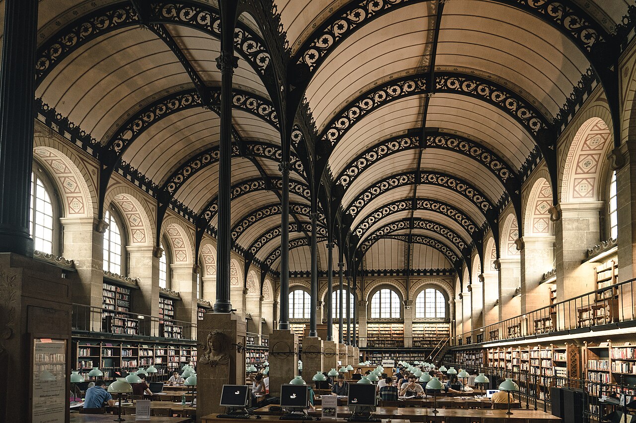 La salle de lecture de la bibliothèque Sainte-Geneviève à Paris, ses longues tables et ses rayonnages sous une voûte