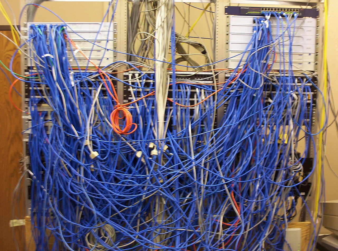 Un local technique où convergent des dizaines de câbles réseau branchés sur des panneaux de brassage